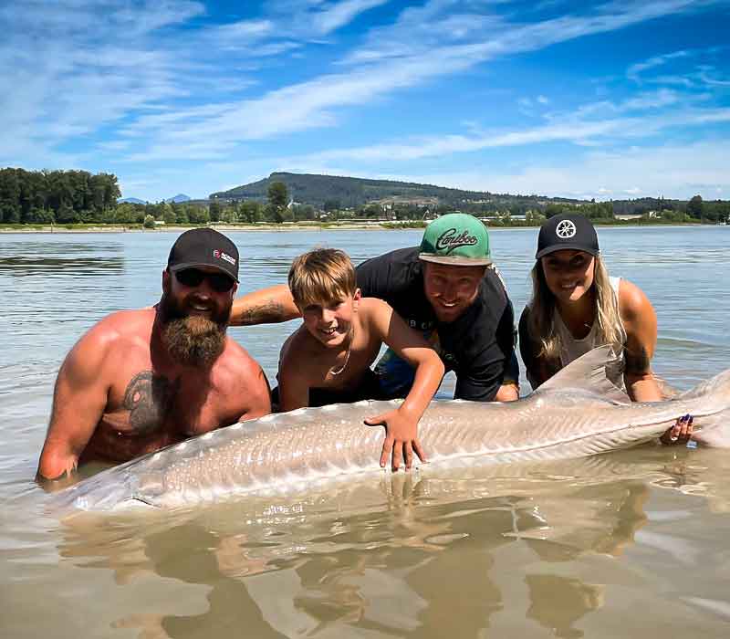 Group of people in the river holding up a Sturgeon they caught