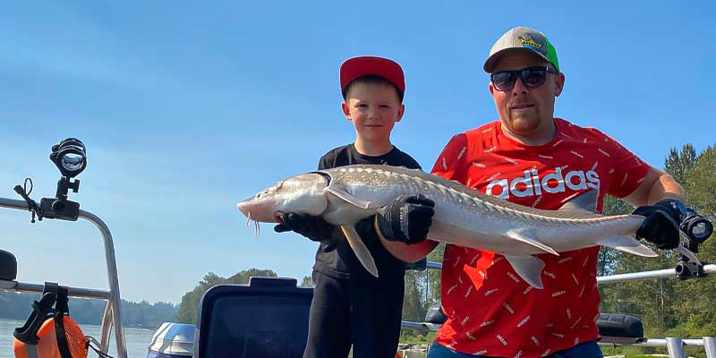 Man and kid holding a sturgeon they caught.