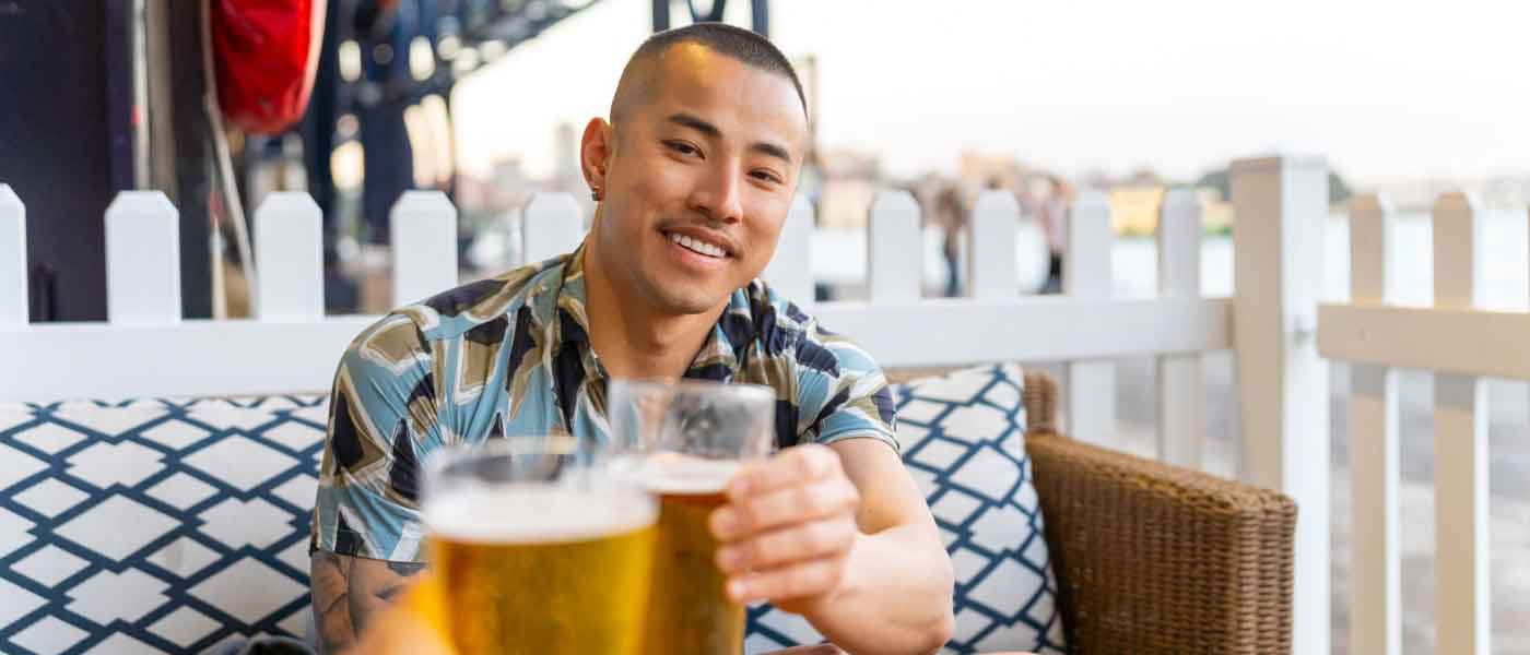 Asian Man enjoying a beer with a friend on a deck.